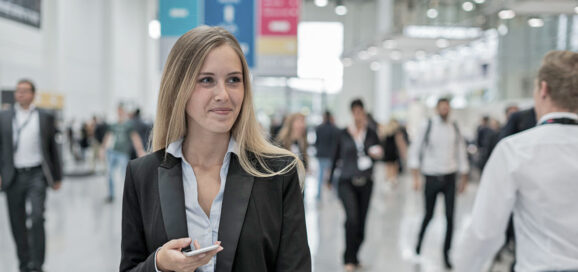 junge Frau auf einer Job-Messe hält Smartphone in der Hand