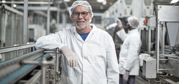 Ein Mann lehnt lächelnd an einer Produktionsanlage