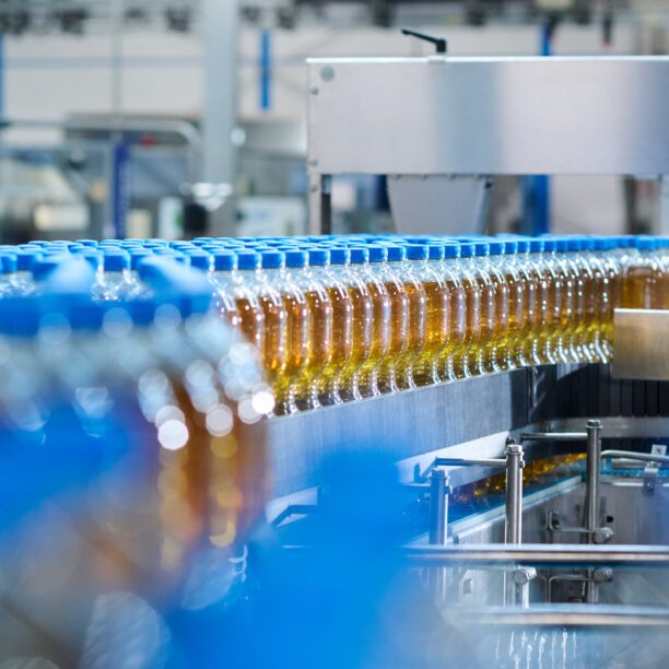 große PET-Flaschen mit orange-braunem Inhalt stehen auf einem Fließband