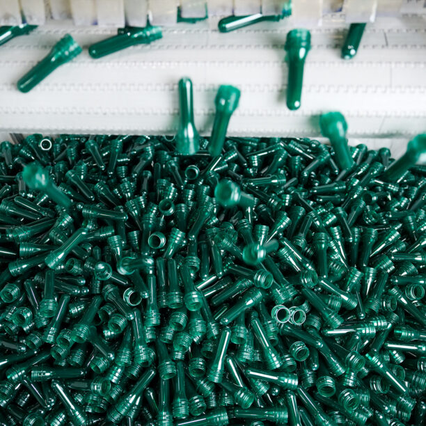 grüne Preforms fallen von einem Fließband in einen großen Auffangbhälter