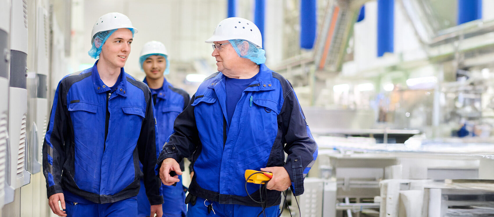 Drei Männer mit Schutzhelmen laufen durch eine Produktionshalle.